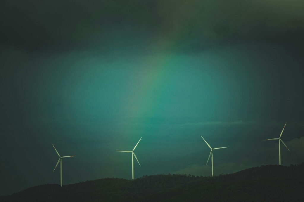Wind turbines on a hill under a dramatic sky with visible rainbow, promoting renewable energy.